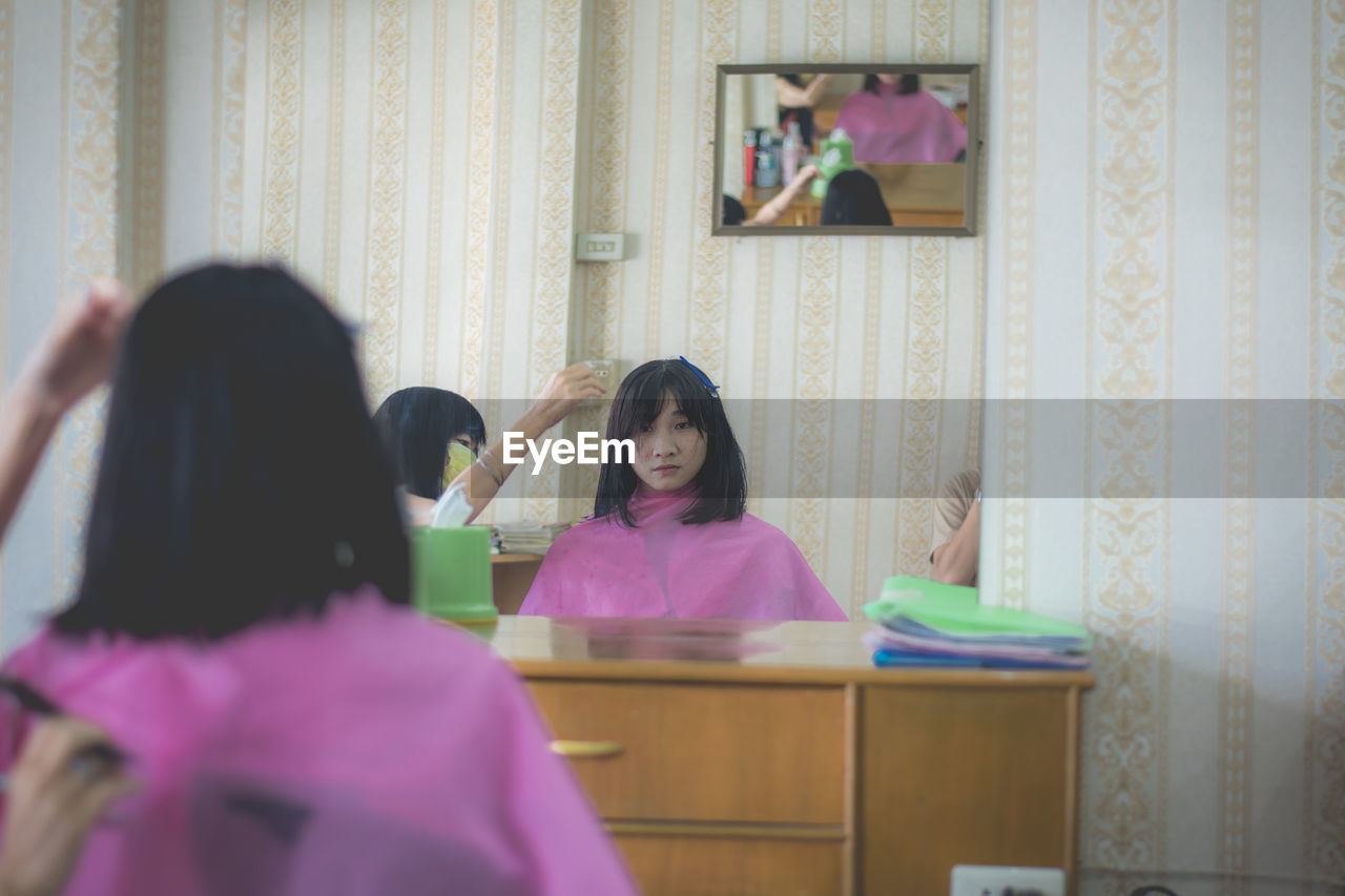 Cropped hands of beautician styling young woman hair in salon