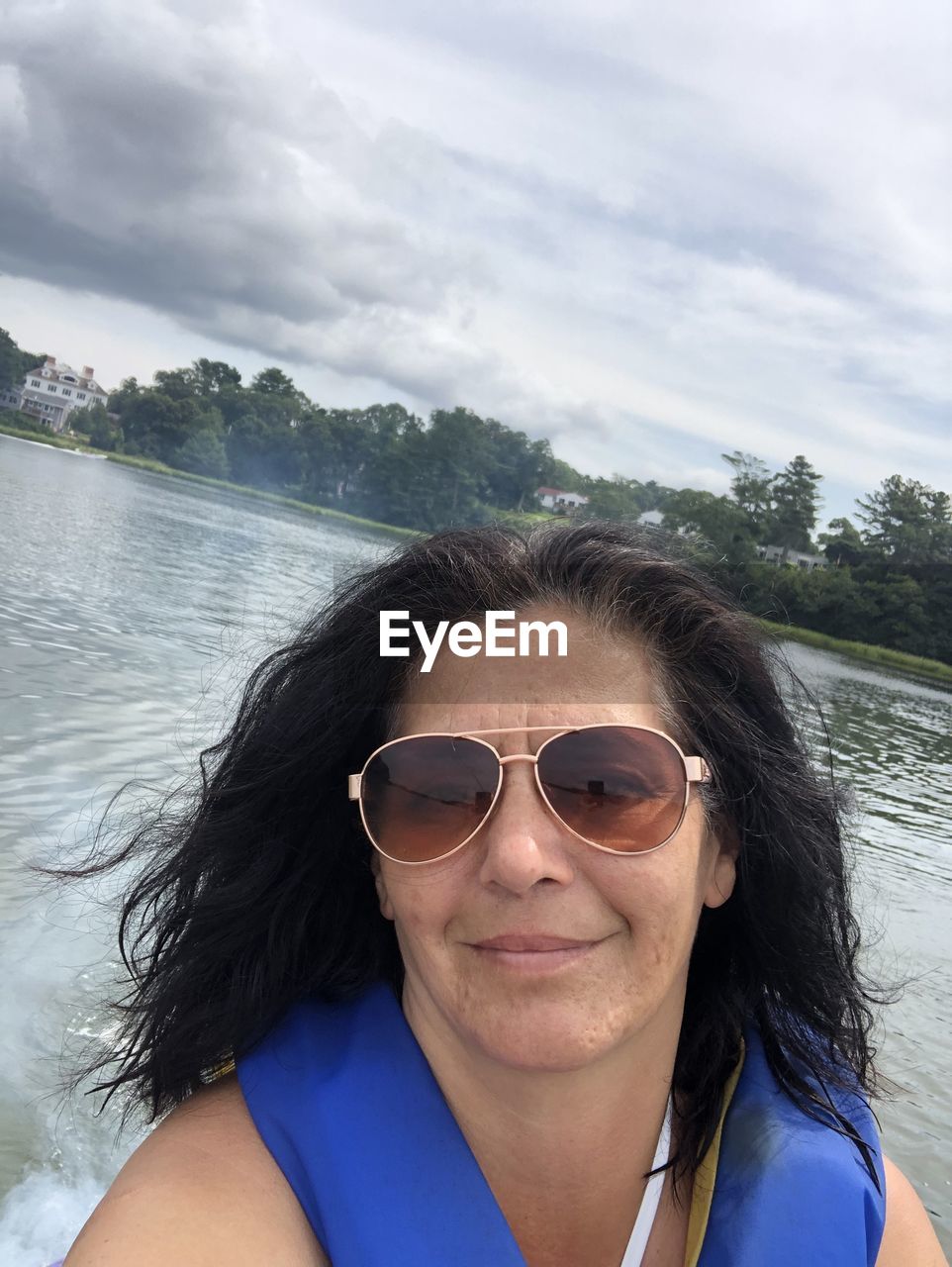 Portrait of woman wearing sunglasses against lake and sky
