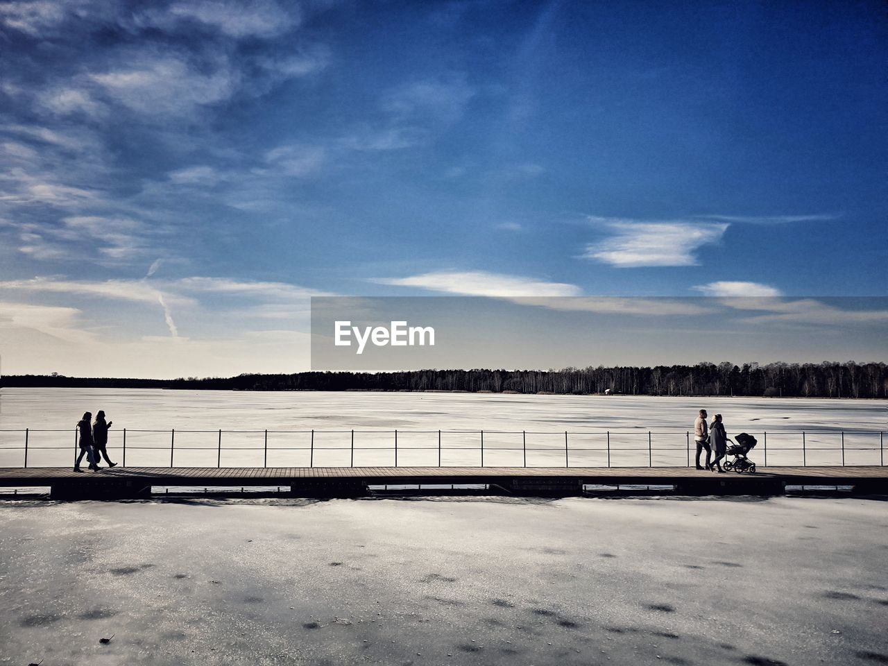 People walking on pier over frozen lake during winter