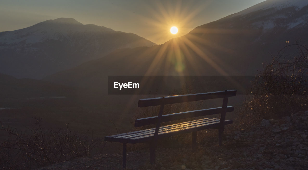 Empty bench on mountain against sky during sunset
