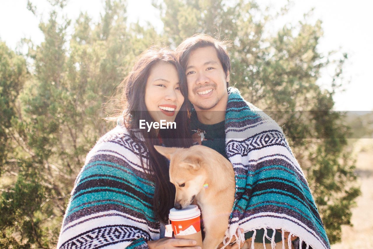 Portrait of a smiling couple with dog covered in blanket