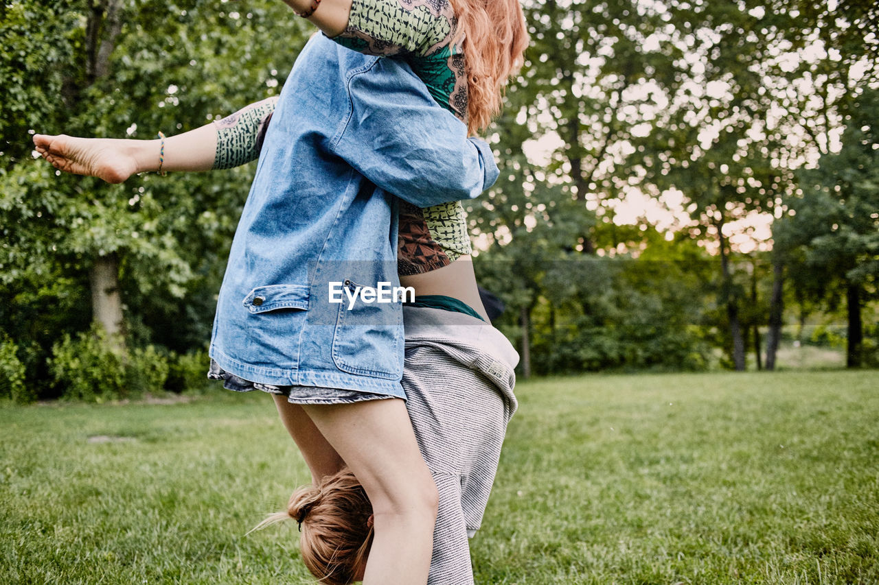 Midsection of woman assisting friend in doing handstand on field