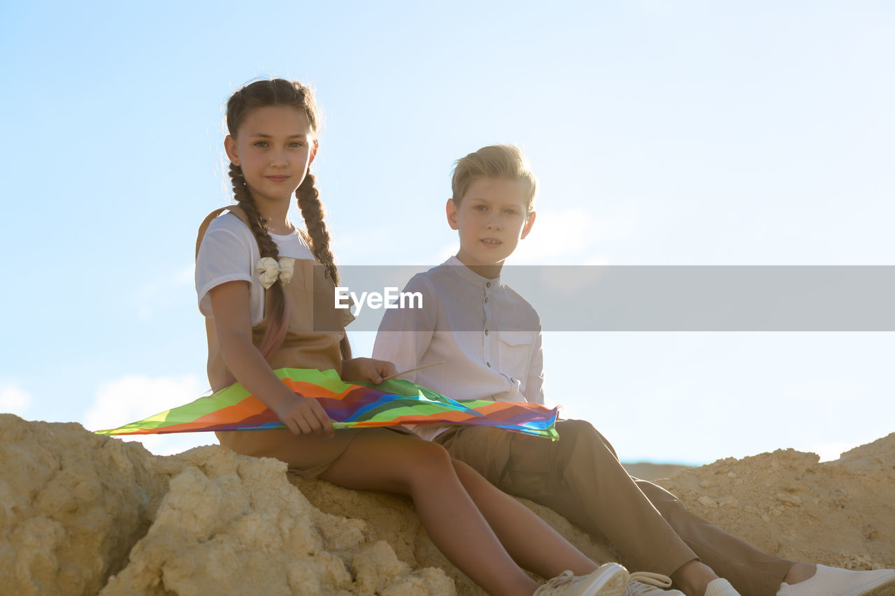 Teenage children are sitting on a high mountain thinking how assemble a kite.