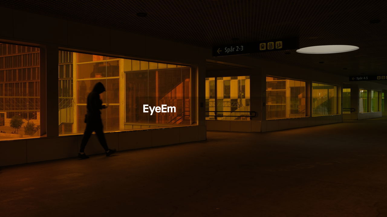 FULL LENGTH OF SILHOUETTE MAN WALKING IN ILLUMINATED BUILDING