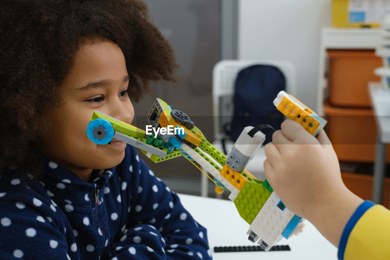Coding class, school girl constructing robot arm mechanism. multiethnic children making science