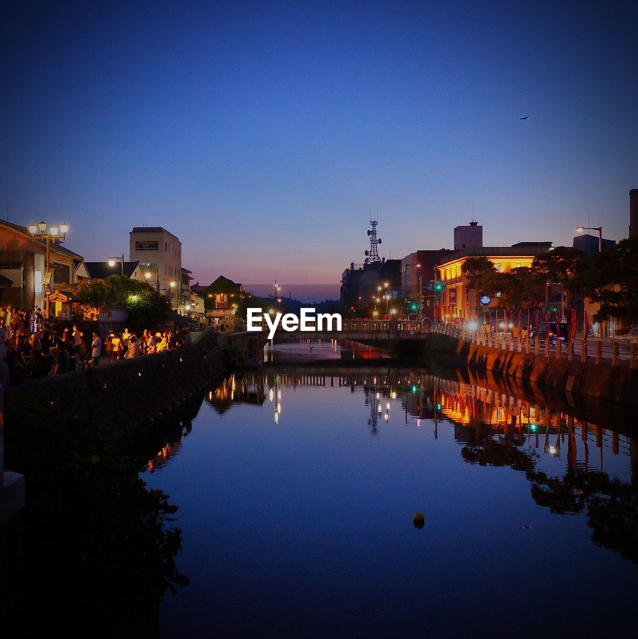 Illuminated buildings by canal against sky