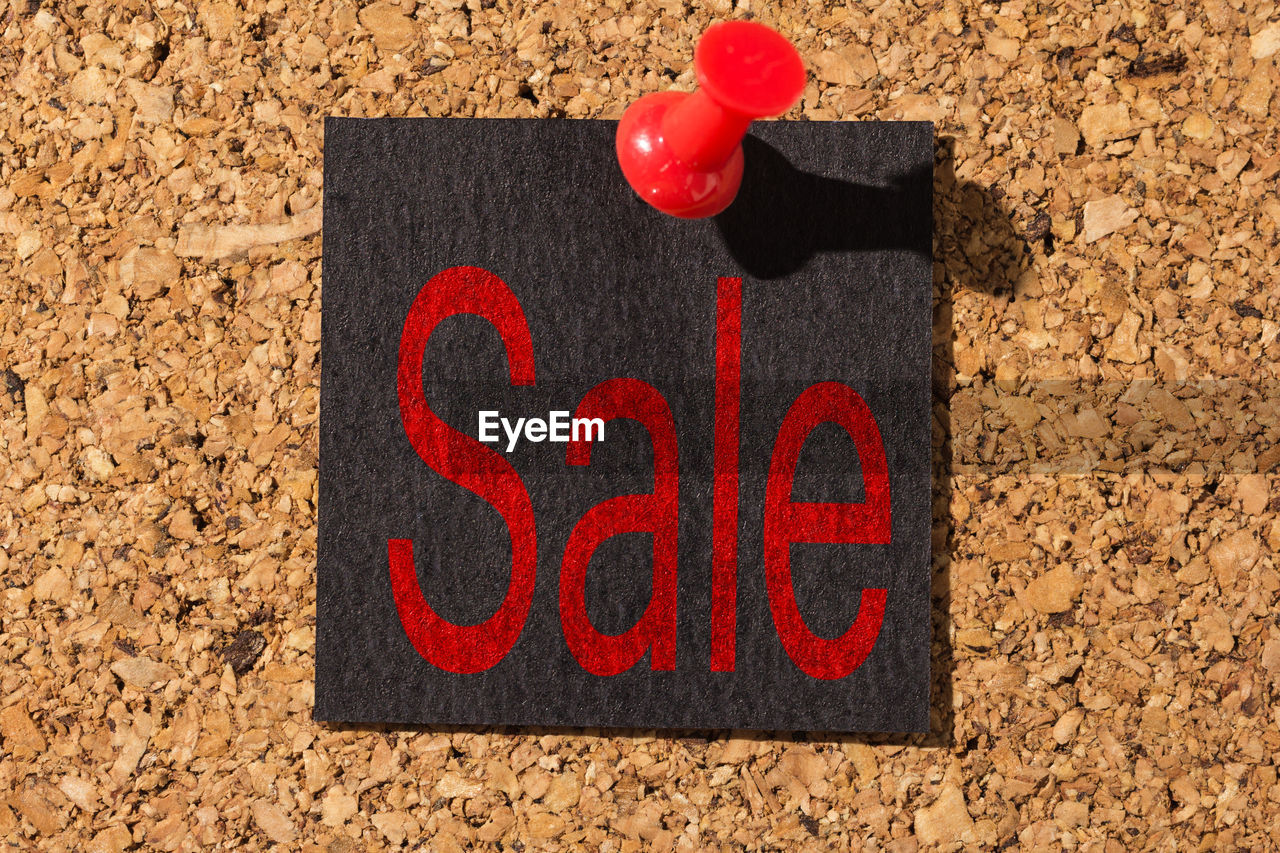 Close-up of paper with sale text pinned on bulletin board