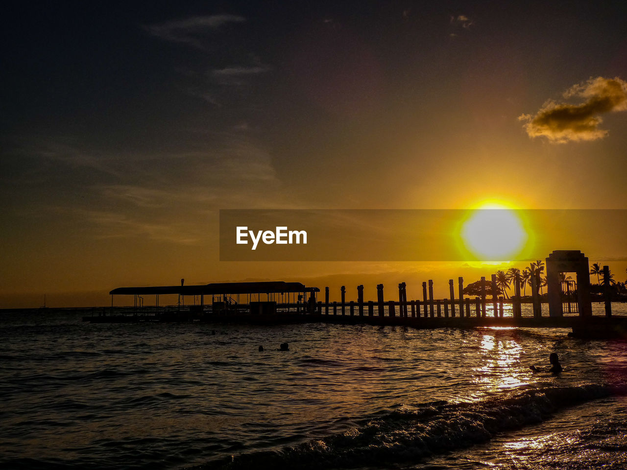 SILHOUETTE WOODEN POSTS IN SEA AGAINST SKY AT SUNSET