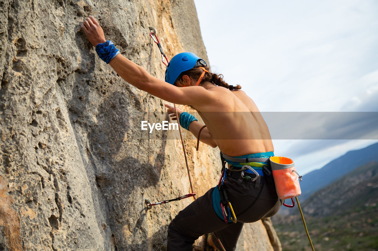 Close-up of shirtless man rock climbing against sky