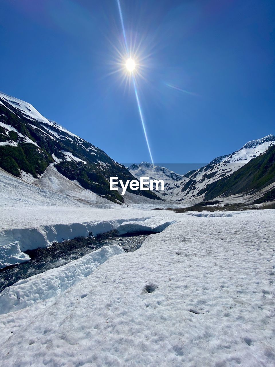 snow, cold temperature, winter, sky, environment, mountain, scenics - nature, landscape, beauty in nature, nature, mountain range, sunlight, sun, blue, ice, frozen, snowcapped mountain, lens flare, travel, no people, sunny, tranquil scene, tranquility, travel destinations, piste, outdoors, day, clear sky, sunbeam, glacial landform, non-urban scene, land, white, polar climate, extreme terrain, winter sports, cloud