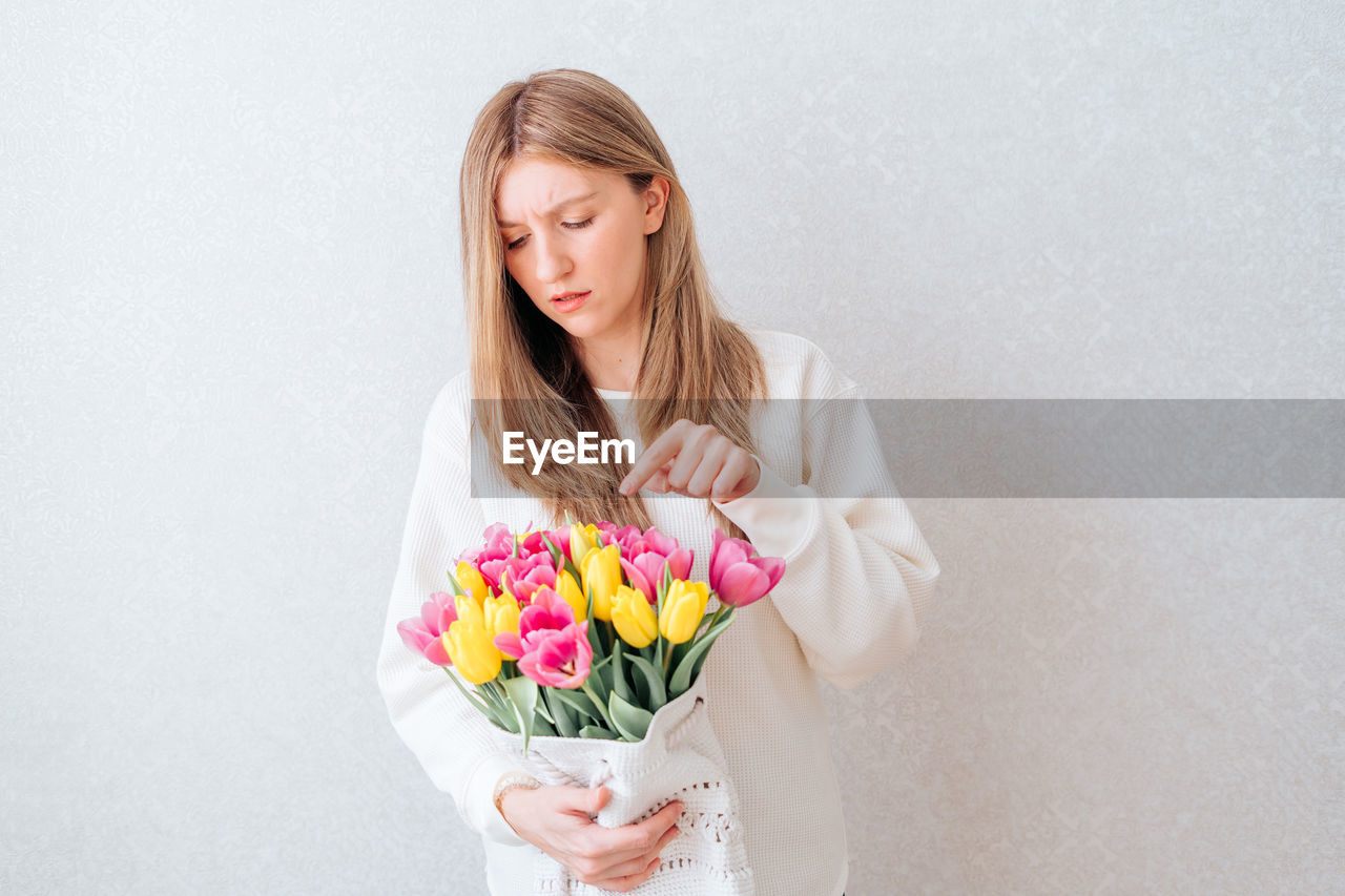 Portrait of sad young caucasian woman holding bouquet tulip flowers. white background, copy space