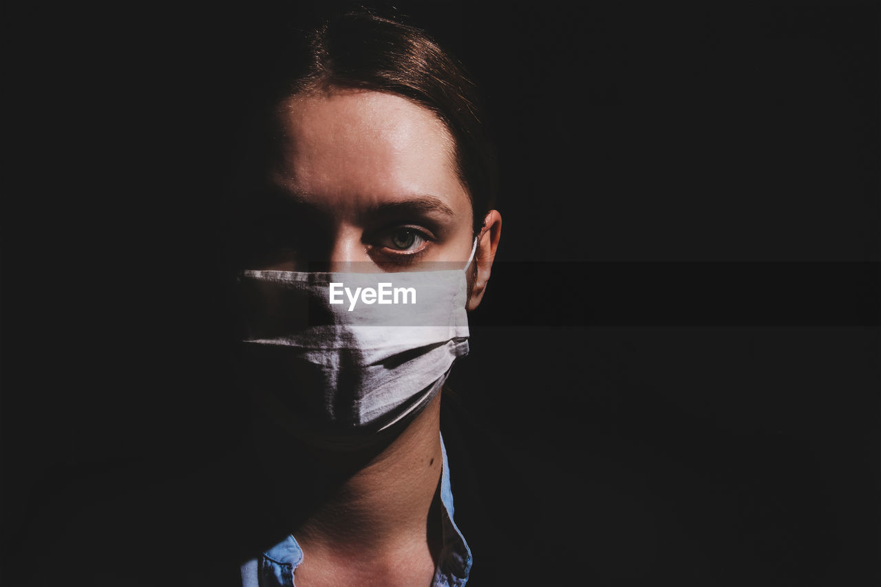 Portrait of young woman wearing mask against black background