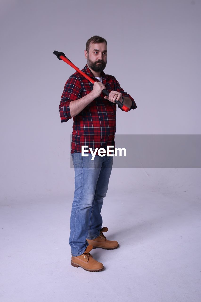 Full length of lumberjack holding axe while standing against white background