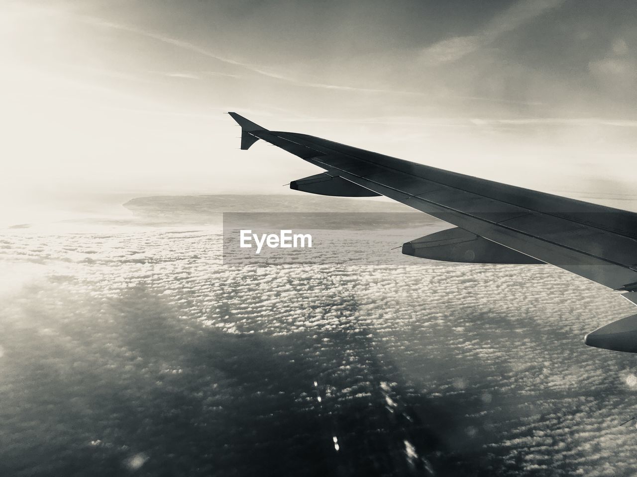Cropped image airplane wing flying over sea against sky