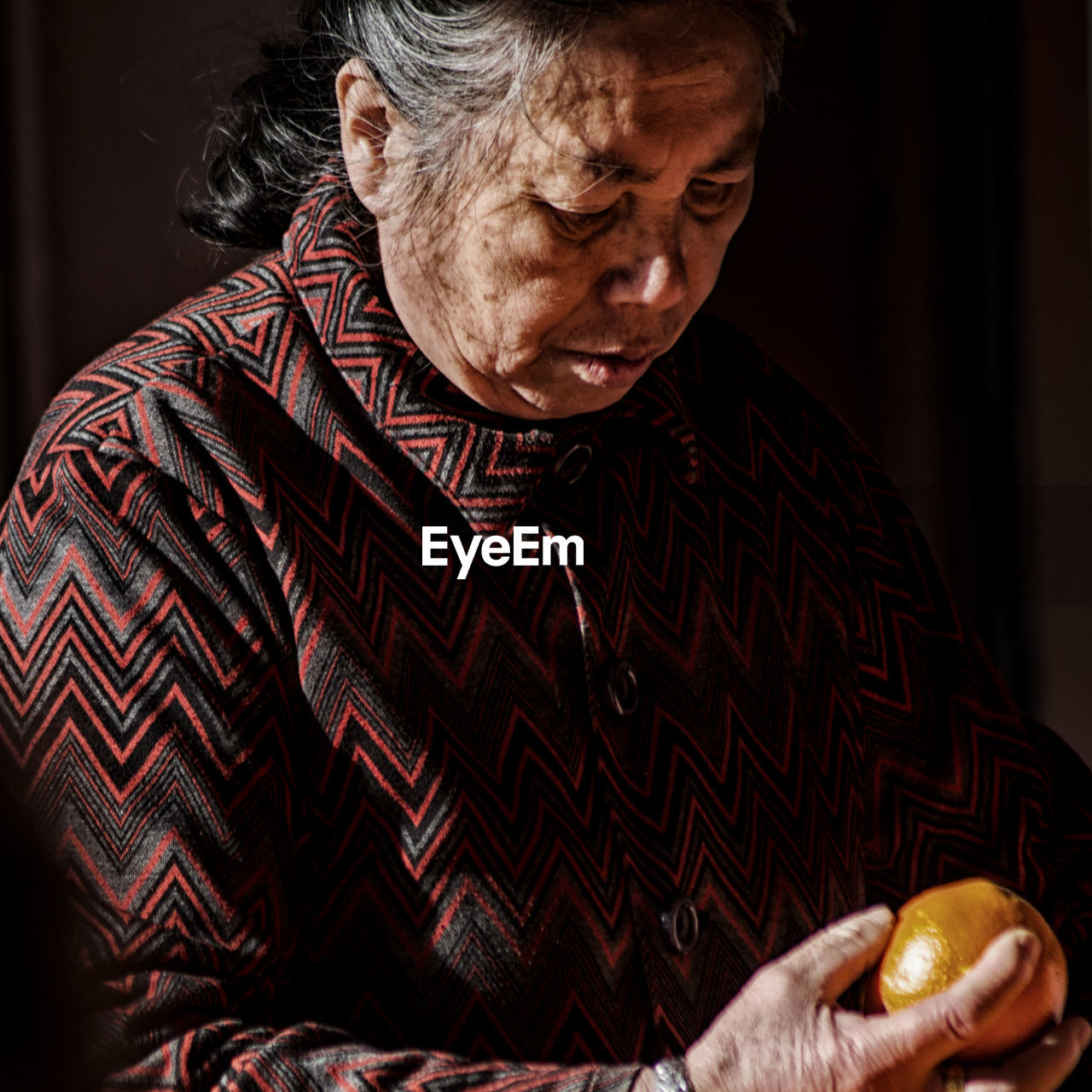 CLOSE-UP OF SENIOR WOMAN HOLDING FRUITS AT HOME