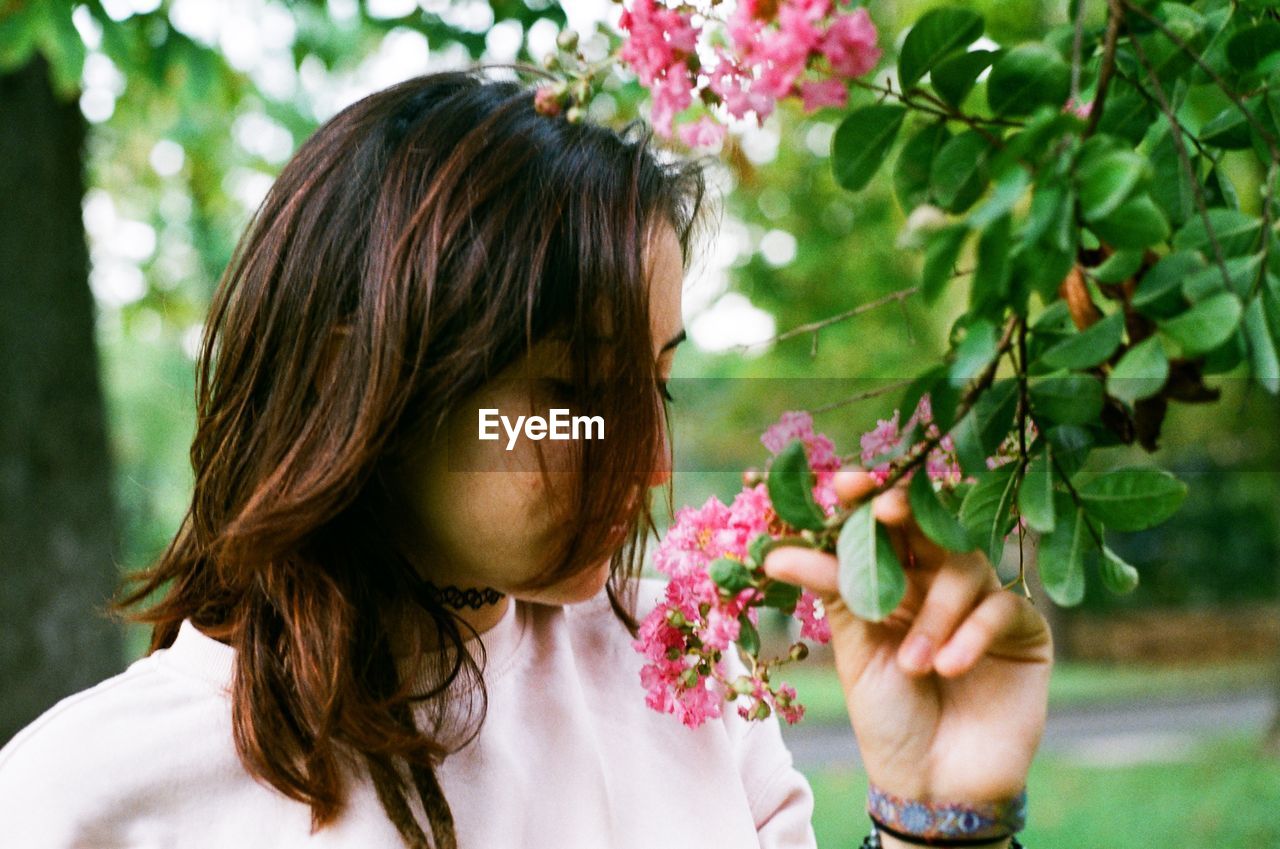 Young woman touching flowers while standing at park