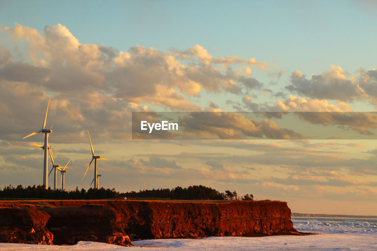 Scenic view of wind turbines by the sea at sunset