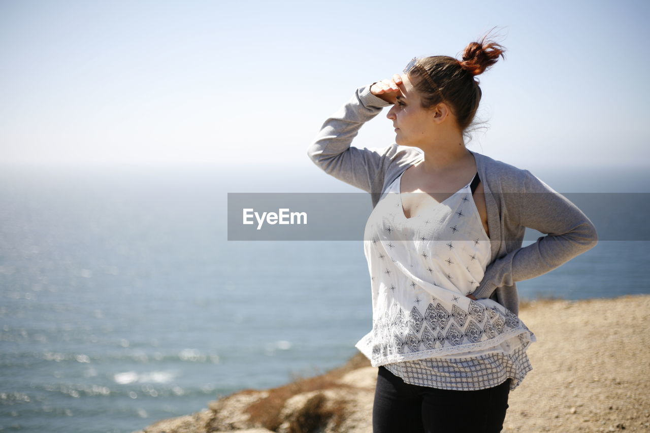 Young woman shielding eyes while standing on cliff