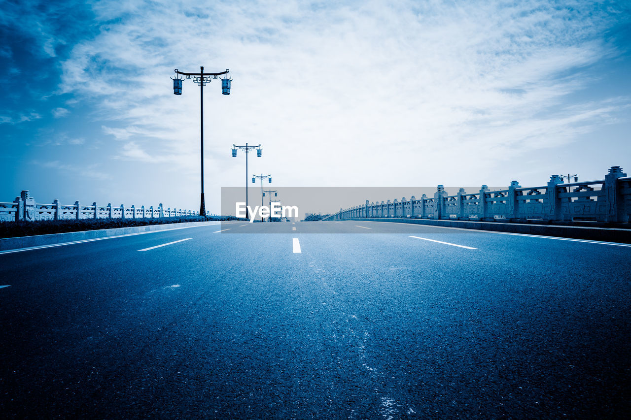 Road leading towards bridge against sky in city