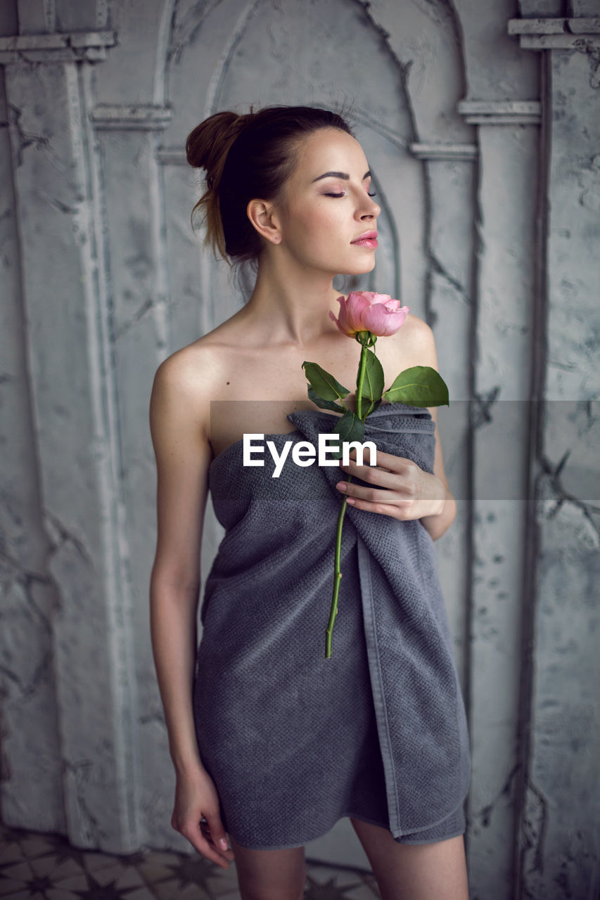 Portrait of a beautiful attractive woman in a gray towel in the bathroom holding a red rose