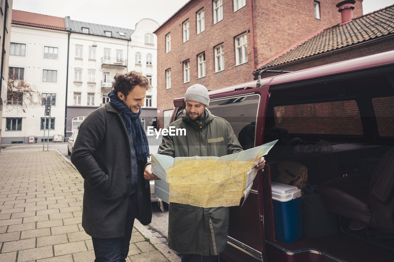 Smiling man examining map with male friend on footpath