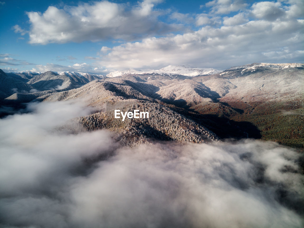 Aerial view, sea of fog and clouds illuminated by the rising sun, snow on the tops of the mountains