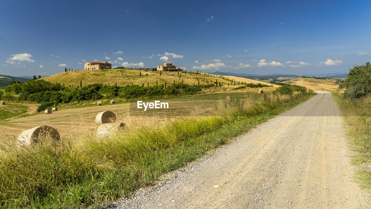 DIRT ROAD AMIDST GRASSY FIELD AGAINST SKY