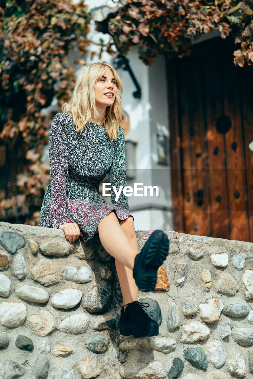 Full length of young woman sitting on retaining wall