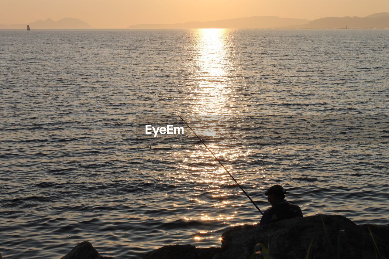 Rear view of man fishing at calm lake