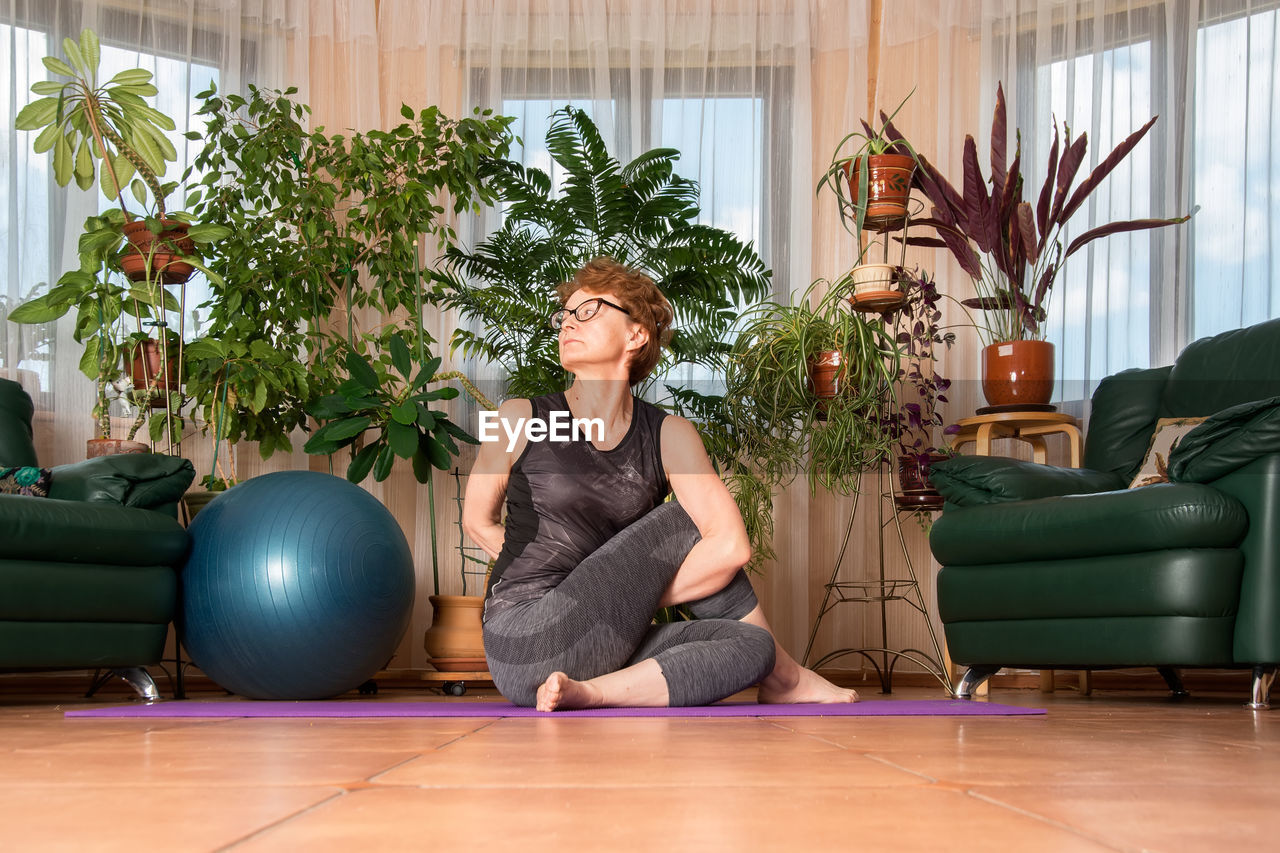 Woman sitting on potted plant at home