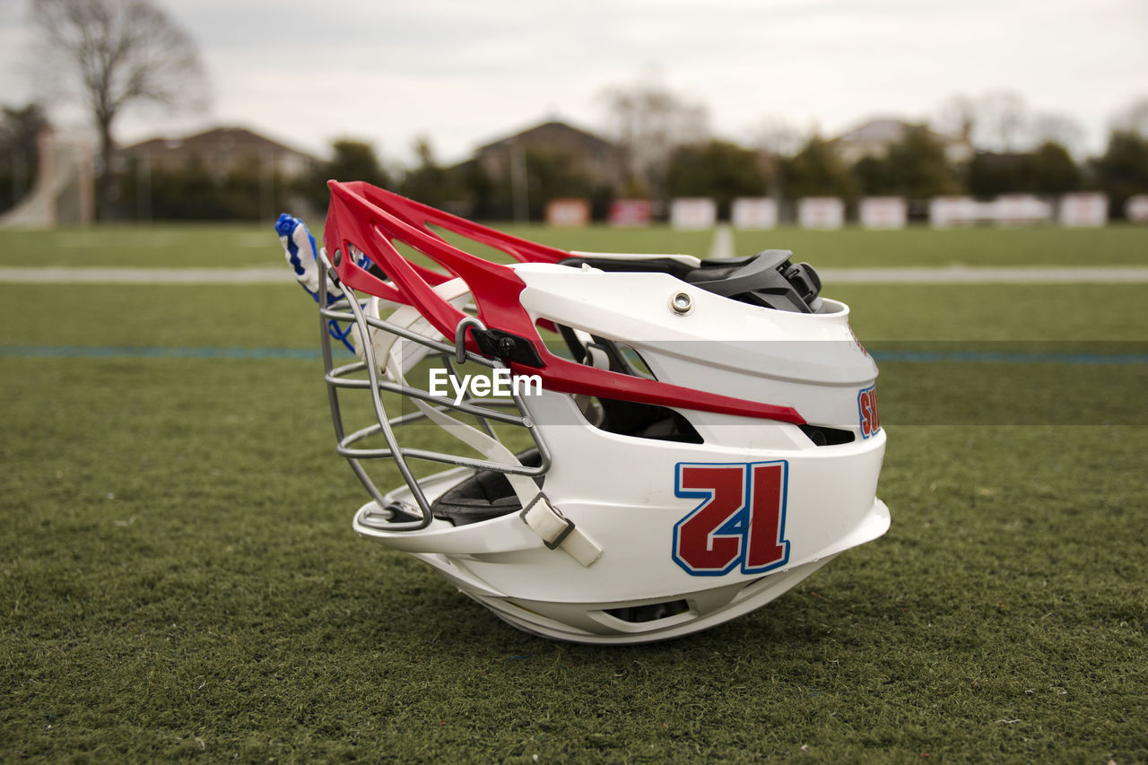 A lacrosse helmet is upside down on a green turf field