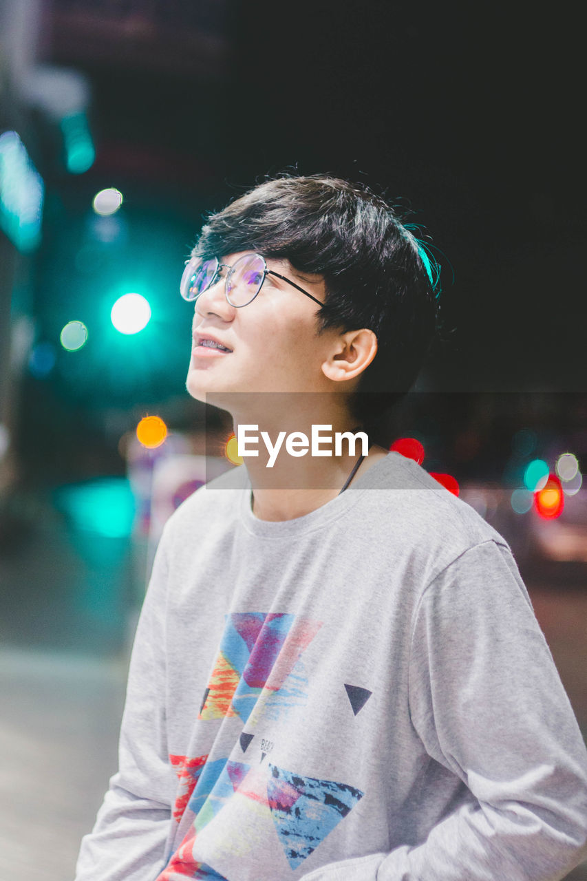 Young man wearing eyeglasses looking away in city at night