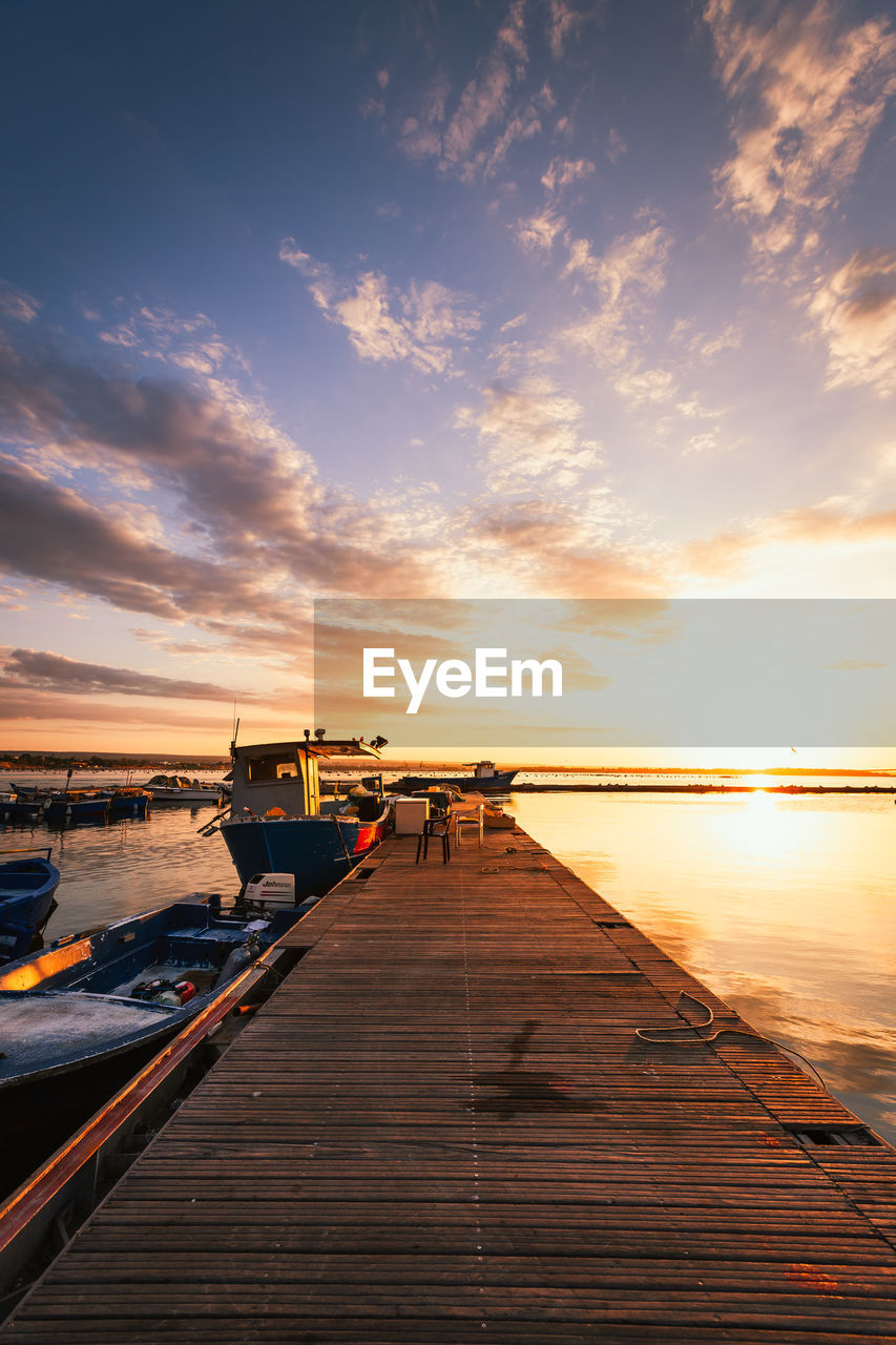 Taranto vecchia pier at dawn with orange sky with clouds and moored boats