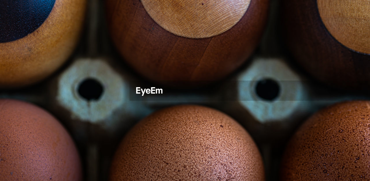 Three fresh eggs close to three wooden eggsmade of pear, oak, wenge and maple wood.