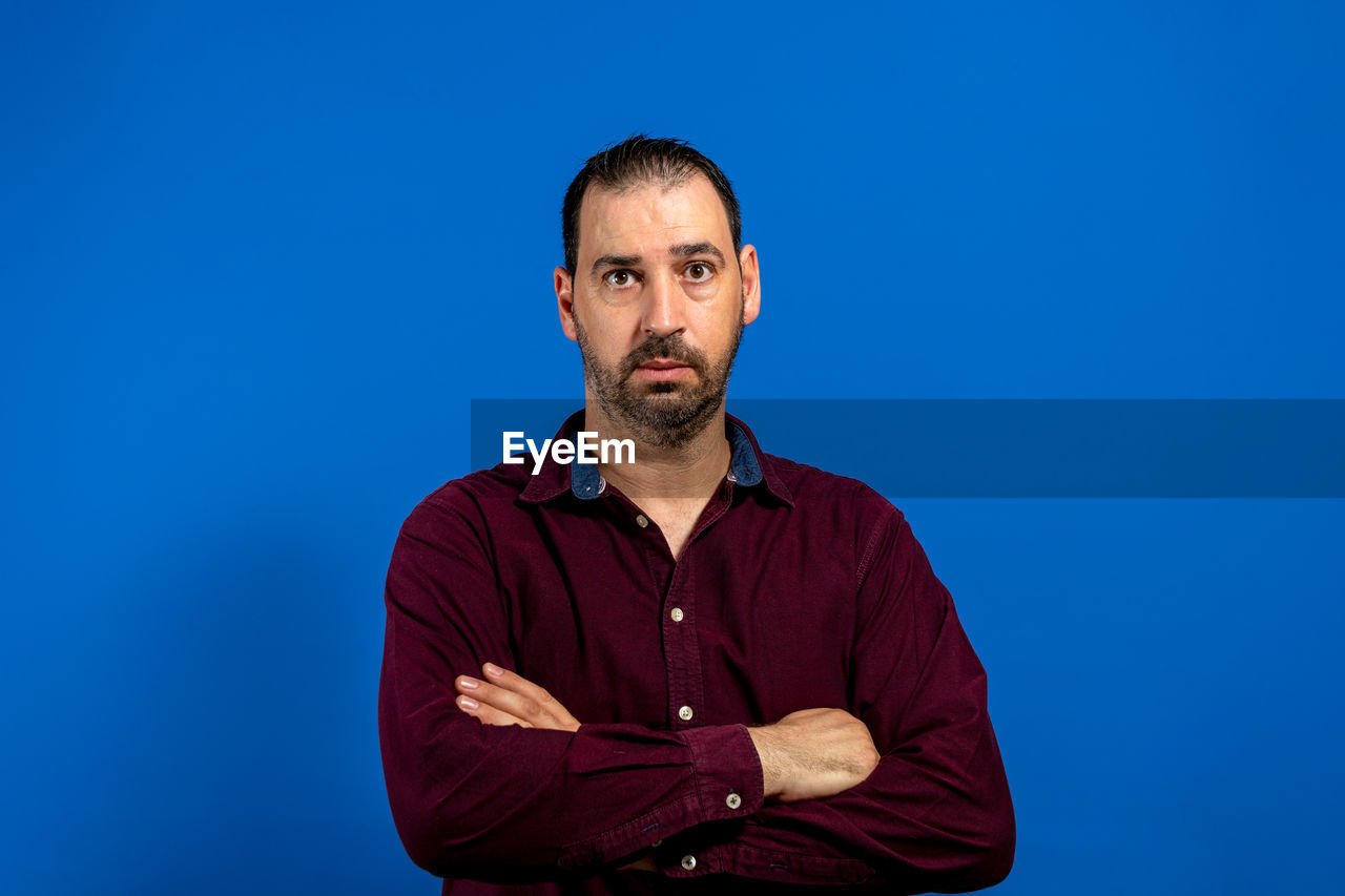 blue, one person, adult, men, portrait, blue background, studio shot, colored background, beard, person, facial hair, looking at camera, waist up, arms crossed, copy space, indoors, front view, casual clothing, serious, human face, clothing, looking, emotion, mature adult, standing, button down shirt, contemplation