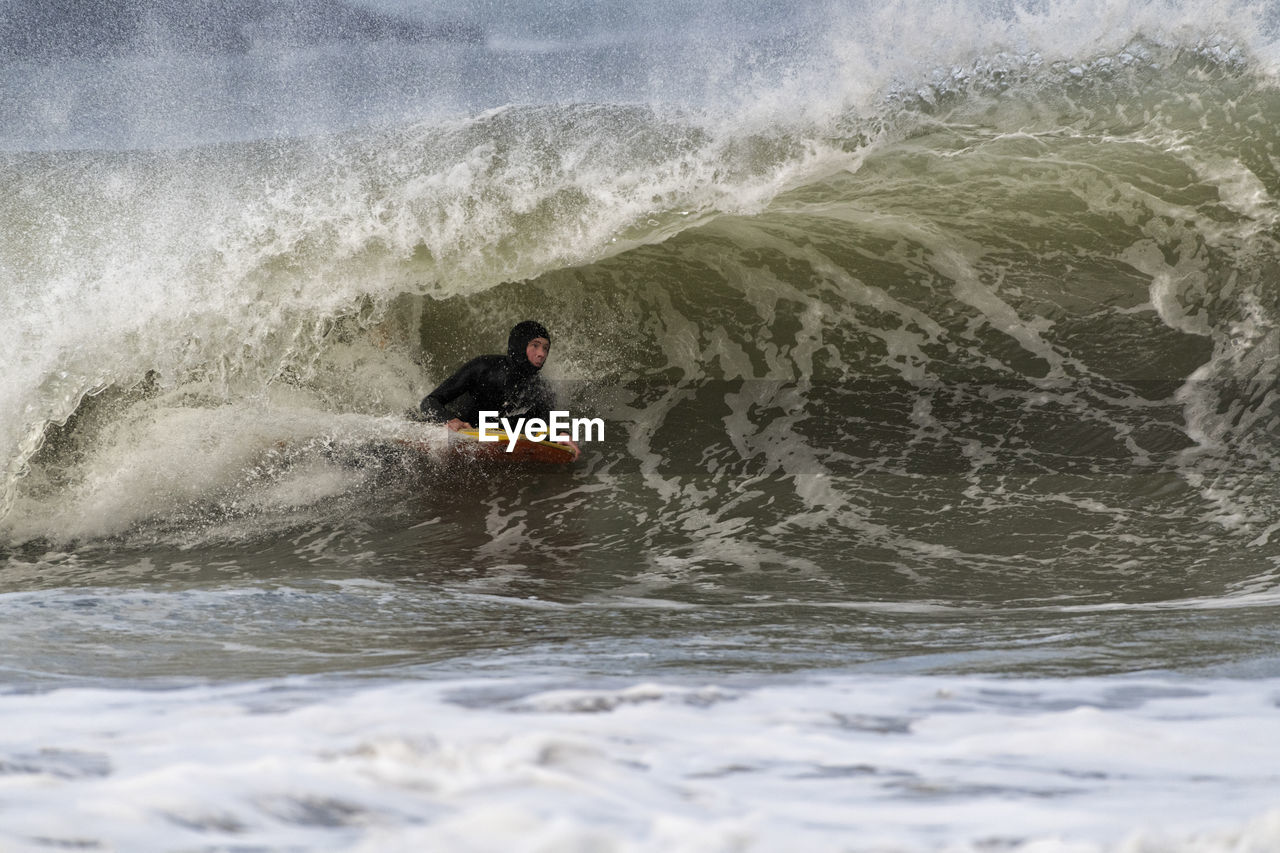 Mature male sportsperson body boarding on waves in sea at broad haven south, uk