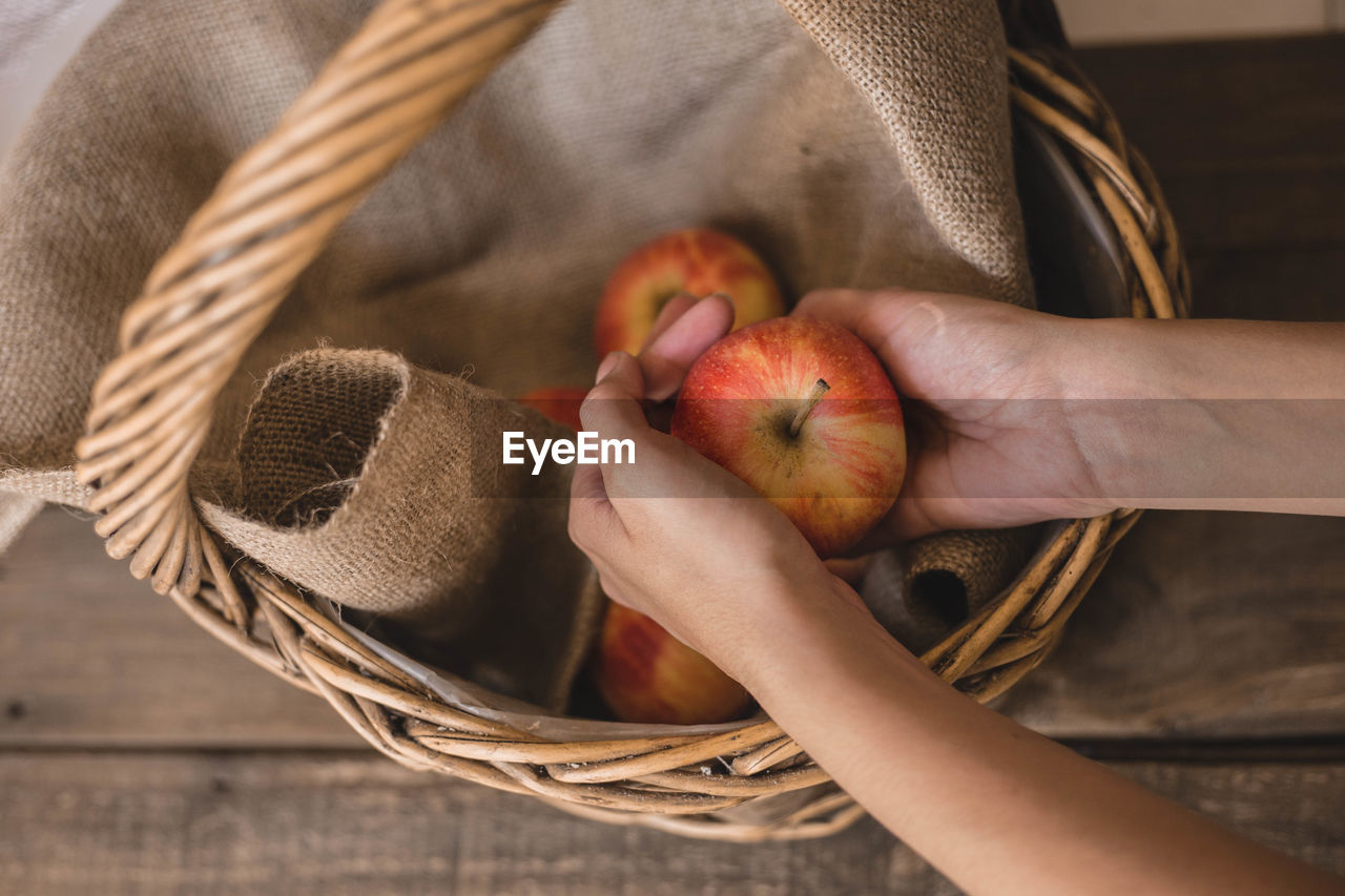 Cropped hands of woman holding apples in basket on table