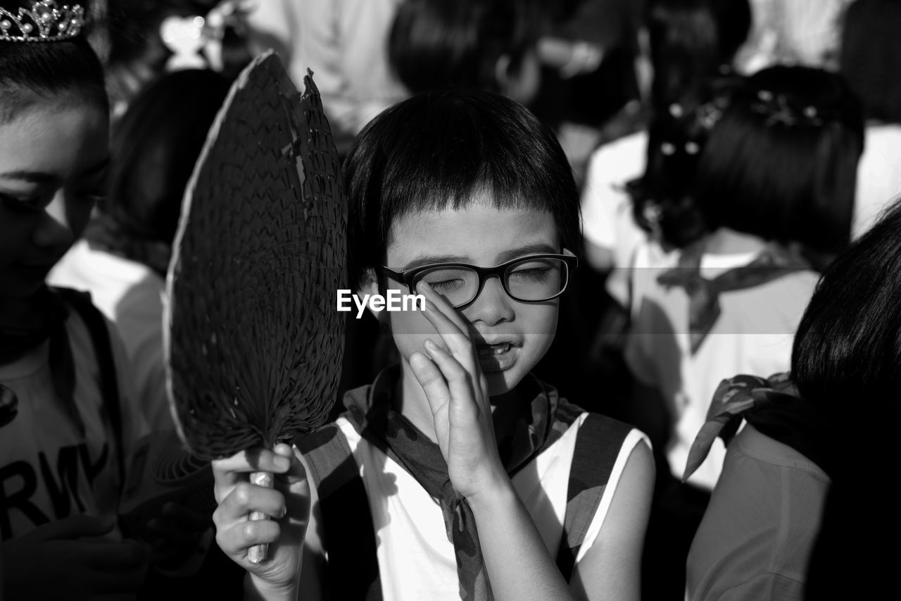 Boy with eyes closed holding hand fan amidst people