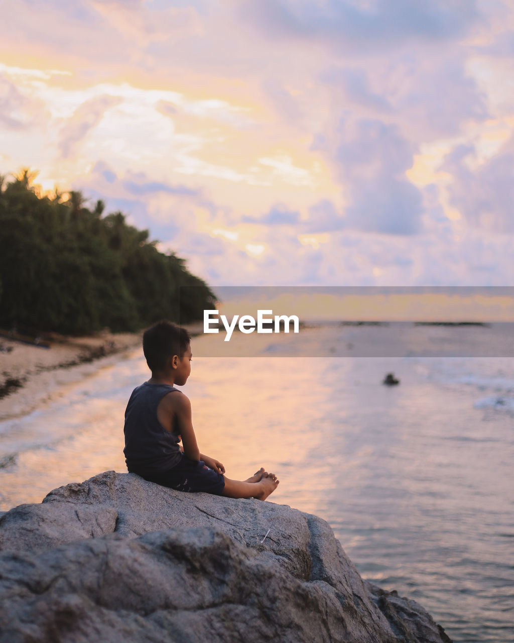 Man sitting on rock looking at sea shore against sky