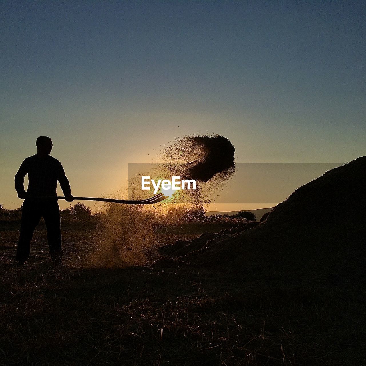 Silhouette man throwing dirt on field during sunset