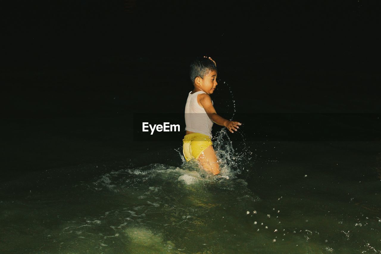 Playful boy dancing in lake against sky during night