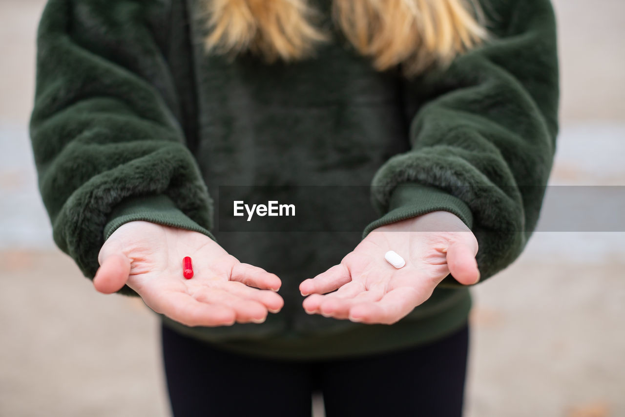 Midsection of woman with red and white pill standing on road