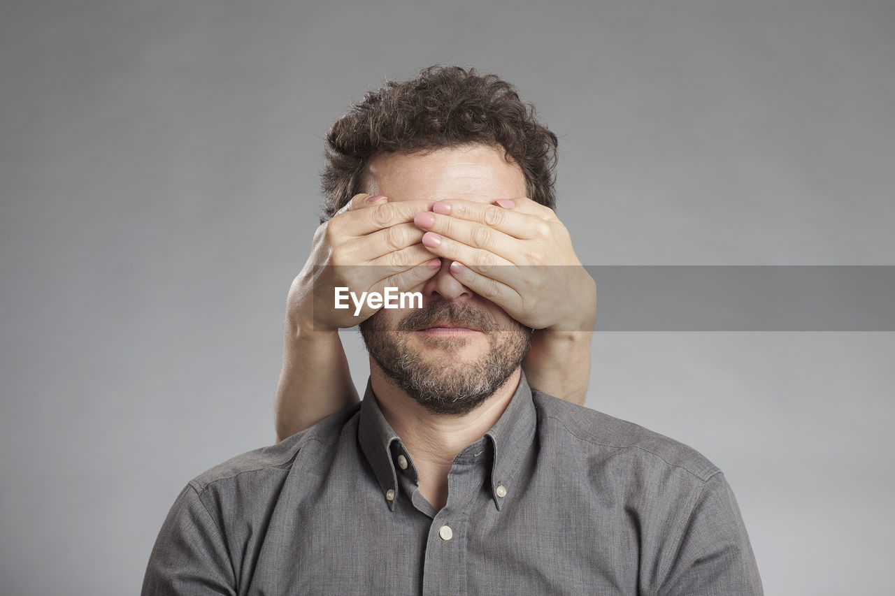 Cropped image of hand covering man eyes against white background