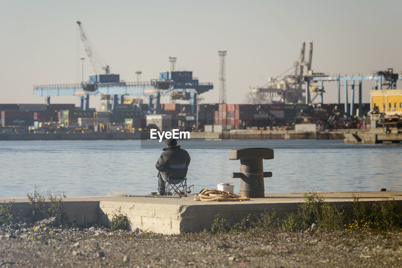 Old fisherman in front of cityscape on the pier of the port of genoa