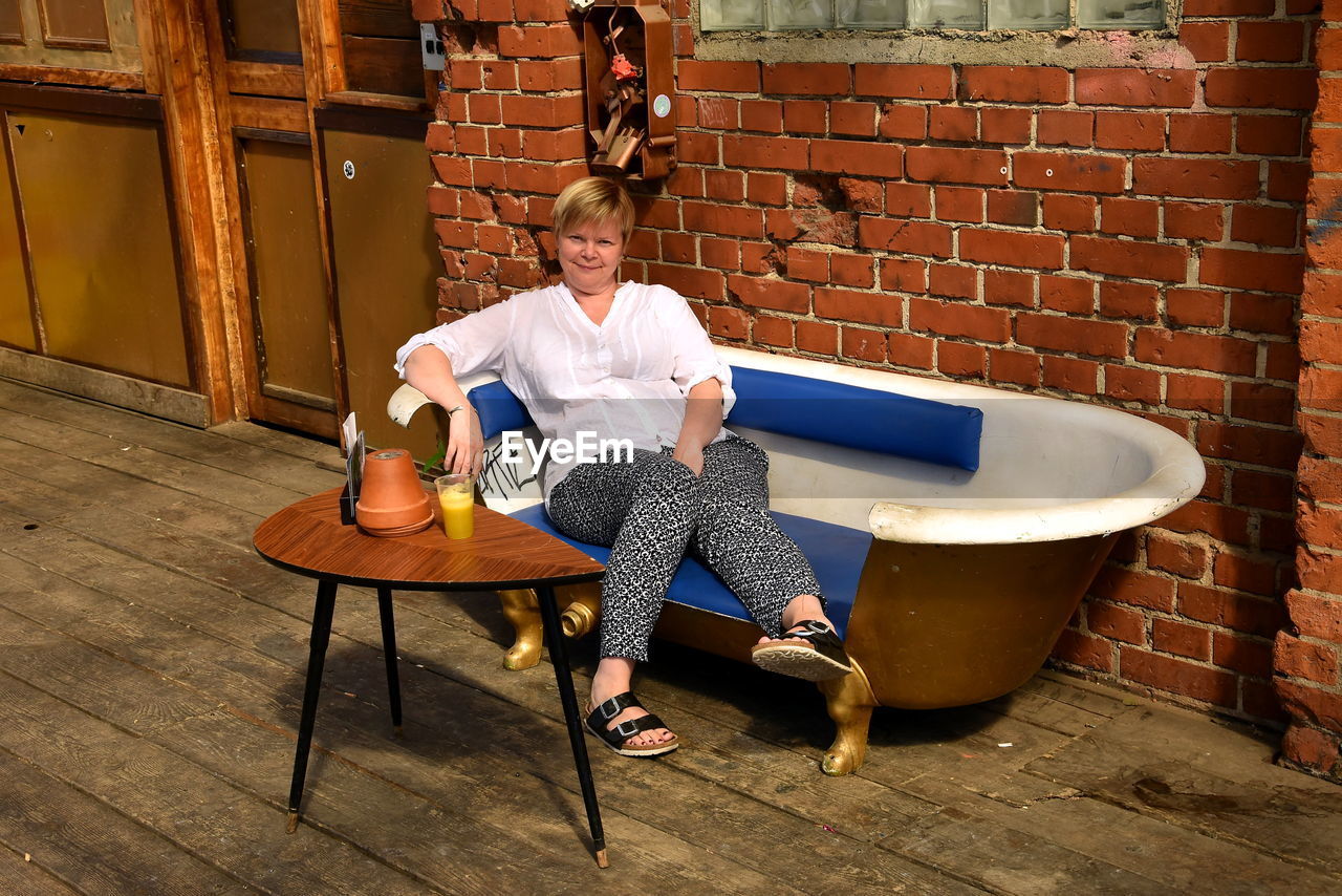 Full length portrait of woman sitting on seat against wall