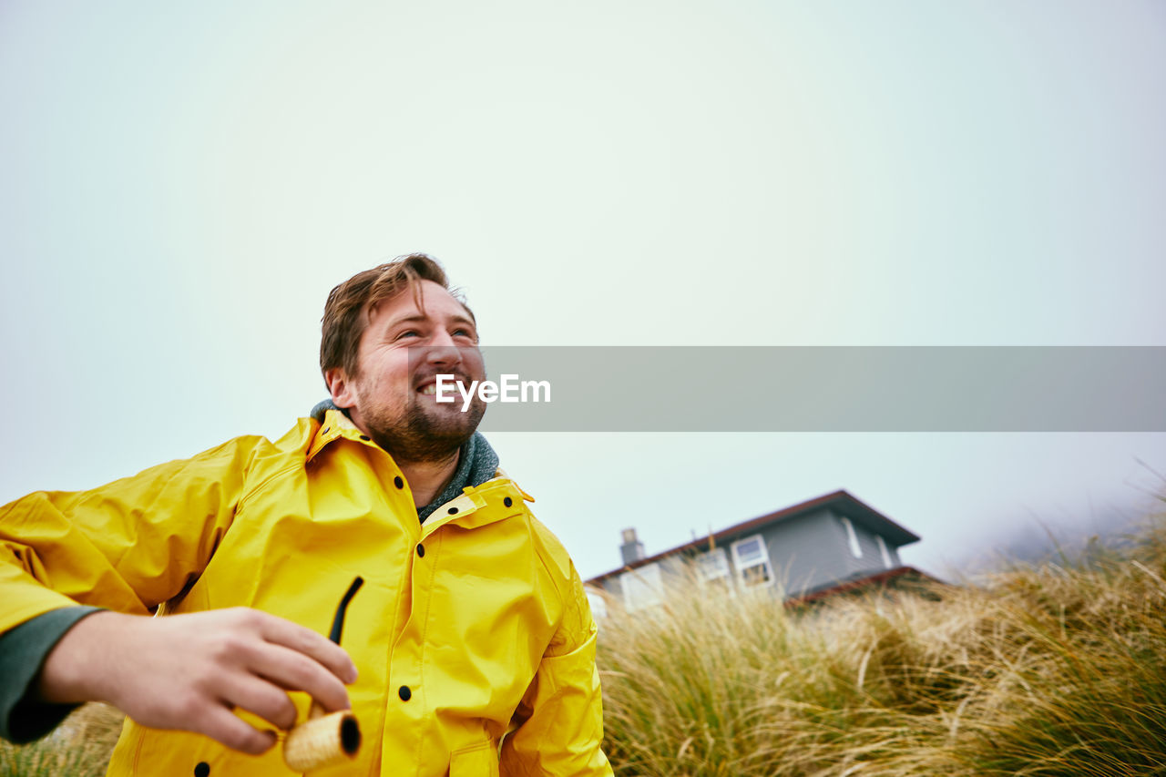 Low angle view of smiling man holding smoking pipe on field against clear sky