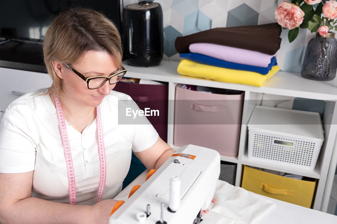 Real middle aged woman tailor sewing clothes using a sewing machine at home. seamstress working.