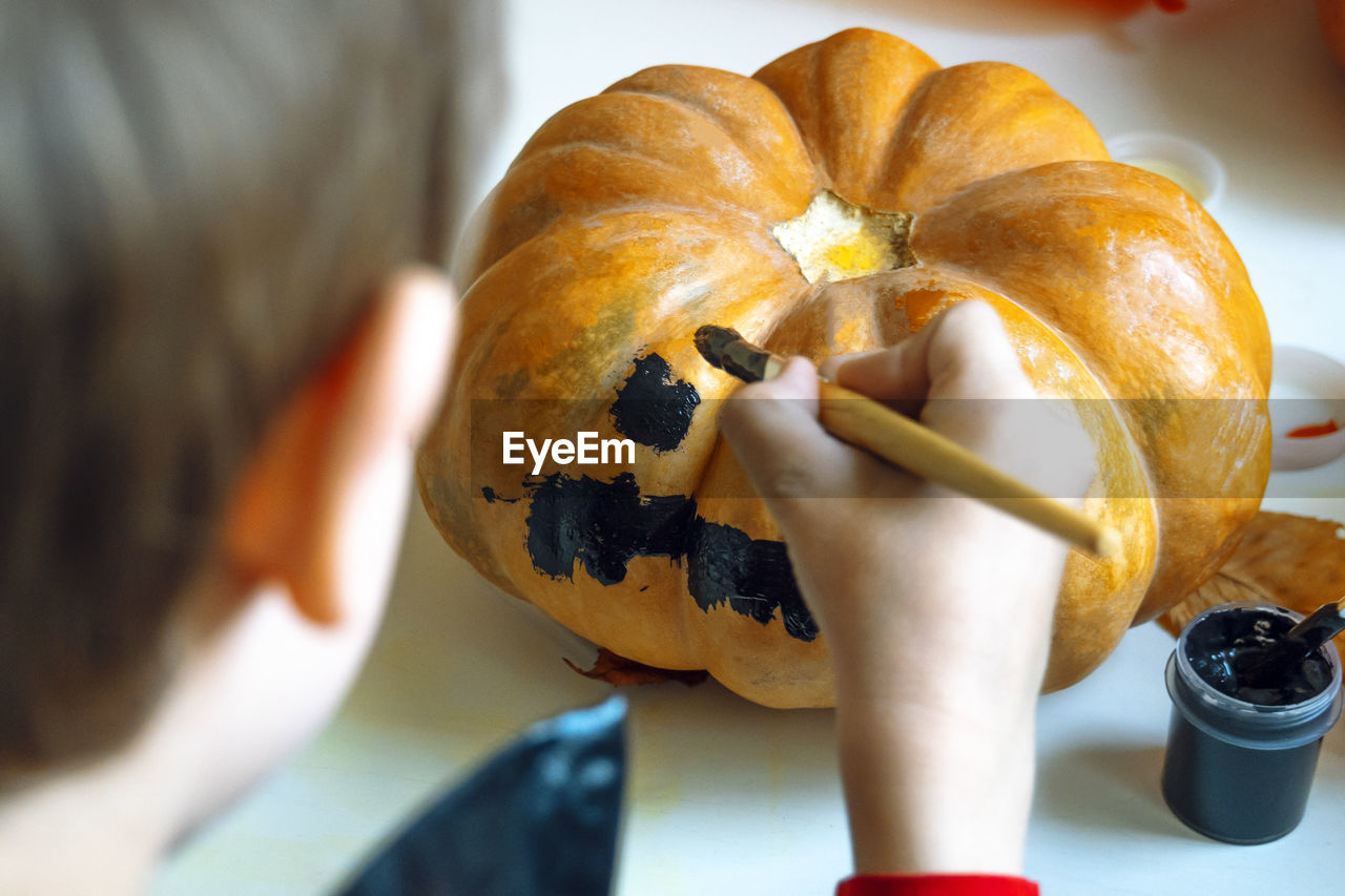 Rear view of boy painting pumpkin at home