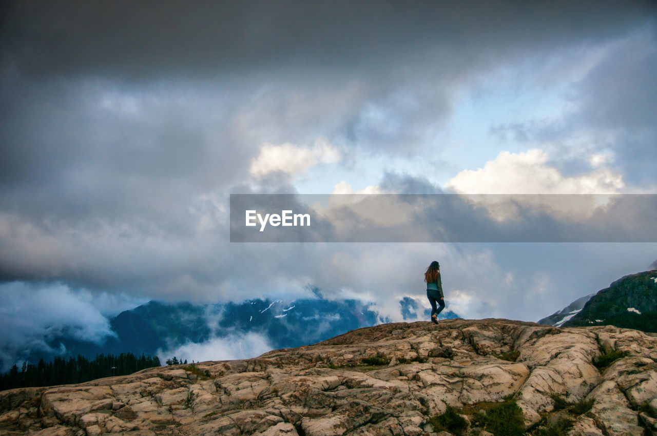Low angle view of woman walking on rocky hill against cloudy sky