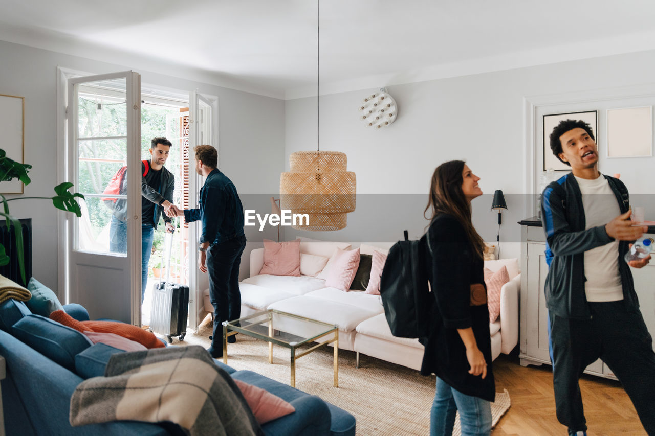 Friends talking in living room while owner handshaking with man at doorway